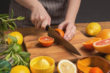 Female hands cutting citrus fruits on wooden board