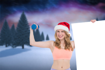 Obraz premium Festive fit blonde smiling at camera holding poster against snowy landscape with fir trees