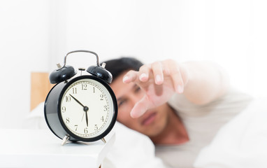 Man's hand is reaching out to alarm clock waking up in early morning