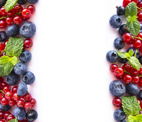 Mix berries and fruits at border of image with copy space for text. Ripe blueberries, red and black currants with mint leaves on white background. Top view. 