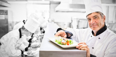 Trainees preparing dishes with head chef presenting salmon dish on counter