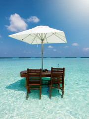 Tisch mit Sonnenschirm und Stühlen in türkisen, tropischen Gewässern