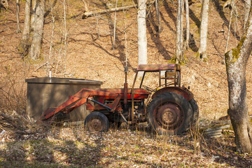 Red old tractor abandoned in a forest