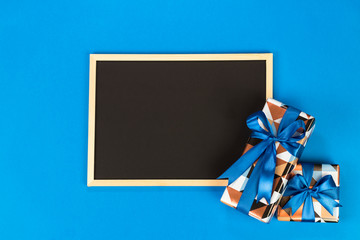 Gift boxes and chalkboard on blue background with copy space.