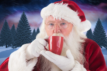 Santa drinks from a red cup against snowy landscape with fir trees