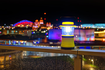 Luminous hand lantern standing on the fence of balcony on the background of illuminated buildings of Sochi Olympic Park, Russia
