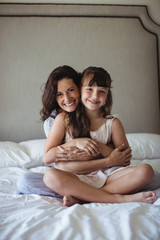 Smiling mother embracing her daughter in bedroom