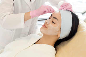 Fototapeta na wymiar Portrait of pretty Asian woman enjoying beauty treatment in Spa with cosmetologist performing facial care procedures
