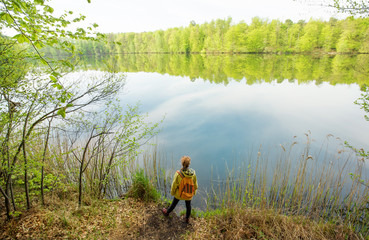 eine Frau steht bei sonnigem Wetter an einem See im Wald