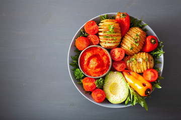 vegan buddha bowl. healthy lunch bowl with hasselback potato, avocado, tomato, bell peppers and pepper sauce