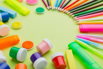 lots of stationery on a green background, multi-colored paints, pencils, markers, eraser, ruler, sharpener, scissors, stapler. The concept of preparing children back to school. Copy space.
