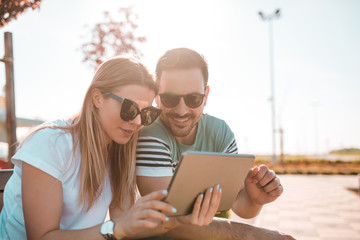 Beautiful girl and her boyfriend, wearing sunglasses and browsing internet on tablet