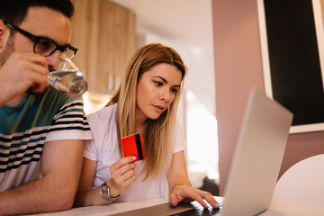 Beautiful girl and her boyfriend are in front of laptop and checking their bank account balance