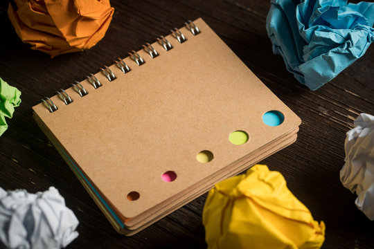 Notizbuch mit verschiedenen Farbmarkierungen und Papierkugeln auf Holzuntergrund
