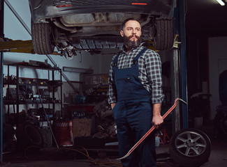 Fototapeta na wymiar Two bearded brutal mechanics repair a car on a lift in the garage. 