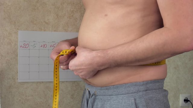 A fat man measures his waist, a big beer belly, a healthy lifestyle