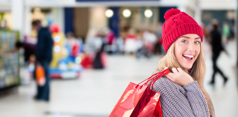 Festive blonde holding shopping bags against shopping mal