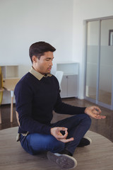 Young businessman practicing yoga at office