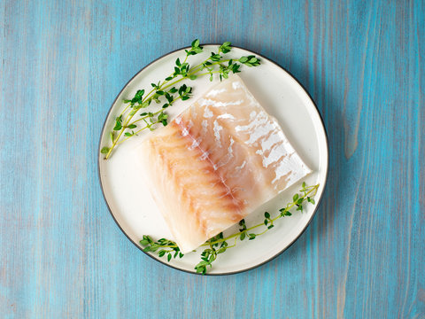 Piece Of Raw Cod Fish Fillet On Plate On Blue Wooden Table, Top View