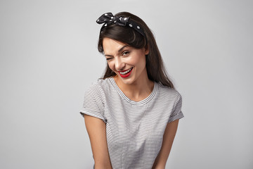 Pretty girl in her twenties winking at camera, smiling playfully. Studio shot of coquettish young brunette woman with bright make up blinking, looking at you with mysterious smile, flirting