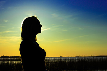 Silhouette of the girl against the background of the sun at the lake in the summer evening