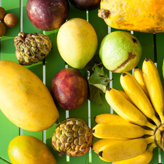 Tropical exotic fruits on a green wooden background.  Custard apple, bananas, lady finger, banana, papaya, mango, longan, lam-yai, rambutan, rambutans.