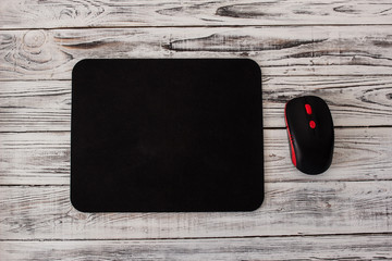 Black computer mousepad with a mouse on a white wooden background
