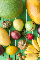 Tropical exotic fruits on a green wooden background.  Custard apple, bananas, lady finger, banana, papaya, mango, longan, lam-yai, rambutan, rambutans.