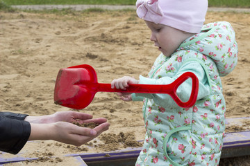 A little girl is playing in the sandbox with her mom, close up