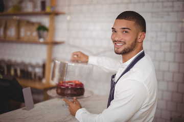 Side view of smiling young waiter holding cake at counter