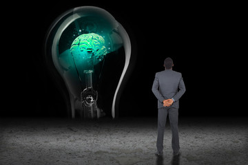 Young businessman standing with hands behind back against glowing brain in light bulb