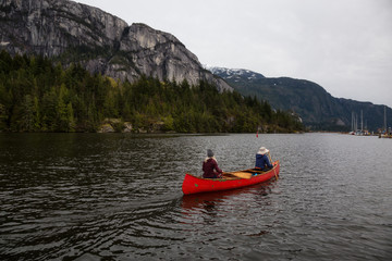 Adventurous people on a wooden canoe are paddling in a river with beautiful rocky mountain in the background. Taken in Squamish, North of Vancouver, BC, Canada.