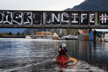 Squamish, British Columbia, Canada - April 15, 2018: Couple friends are canoeing in the river near a train bridge.