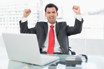 Businessman cheering in front of laptop at office desk