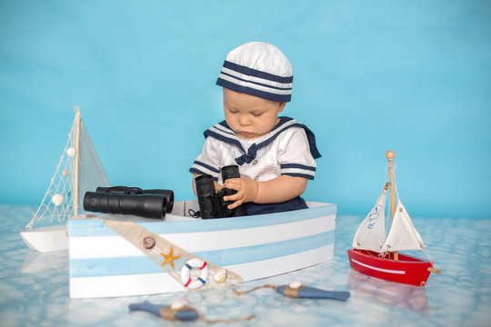 Cute toddler baby boy in wooden boat, playing with fishes, starfish and binoculars as sailman