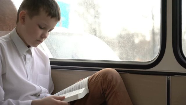 shot of a young schoolboy traveling by bus through city and reads a book.