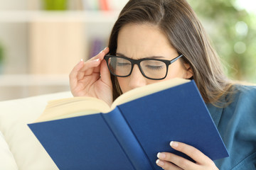 Woman suffering eyestrain reading a book with eyeglasses