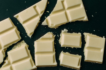 Broken white chocolate bar on black background, top view, macro