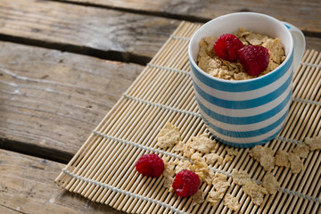 Flakes with raspberries in mug on place mat