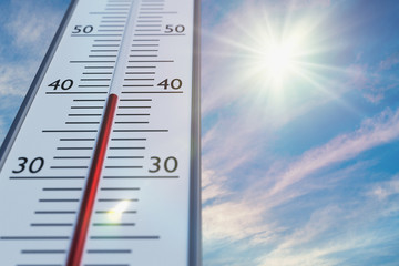 Thermometer against sky with sun in hot weather.