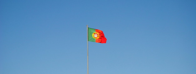 Bandeira portuguesa asteada com vento a bater e com o céu por trás