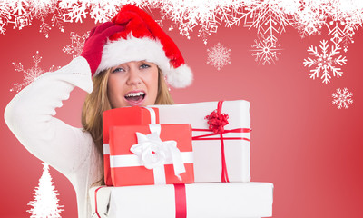 Festive blonde holding pile of gifts against fir tree silhouette over red