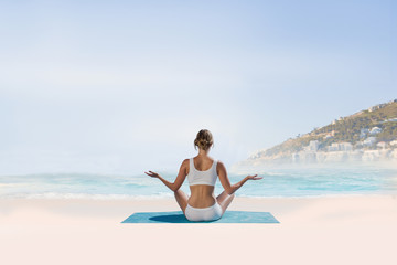 Fit woman sitting in lotus pose  against beautiful beach and blue sky