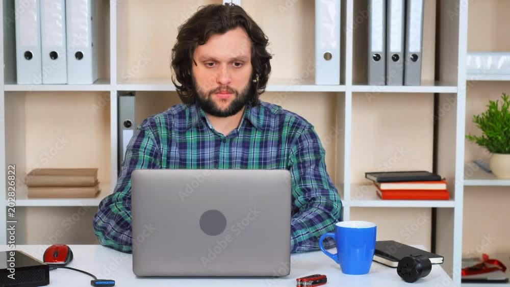 Poster bearded man working in casual office typing on laptop showing hand gesture like. smiling worker sitt