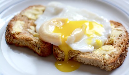 Runny poached egg on brown buttered toast