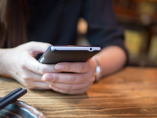 Happy young woman eating sushi in a restaurant and using mobile phone