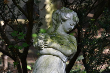 Fototapeta na wymiar With moss covered sculpture of a woman on a tomb of the cemetery in Berlin-Charlottenburg