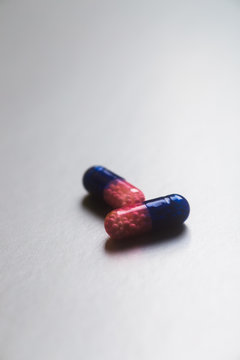Closeup two dark blue and pink transparent capsules with micro-granules inside on light background