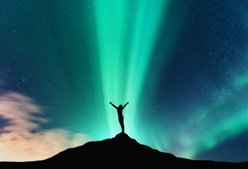 Aurora and silhouette of standing woman with raised up arms on the mountain in Norway. Aurora...