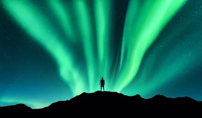Poster Aurora borealis and silhouette of standing man. Lofoten islands, Norway. Aurora and happy man. Sky with stars and green polar lights. Night landscape with aurora and people. Concept. Nature background © den-belitsky